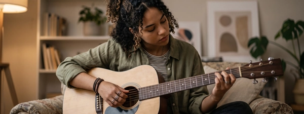 A young woman playing an acoustic
        guitar at home, symbolizing the emotional regulation, resilience, and personal growth achieved through
        specialized counseling and therapy services for children, teens, and adults.